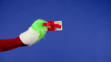 Yeşil saçlı Grinch el, izole bir arka planda kırmızı bir fiyonka sarılı bir tomar para tutuyor. Reklamınız için bir yer. Noel ve yeni yıl kutlaması konsepti. Mavi ekran, krom anahtar
