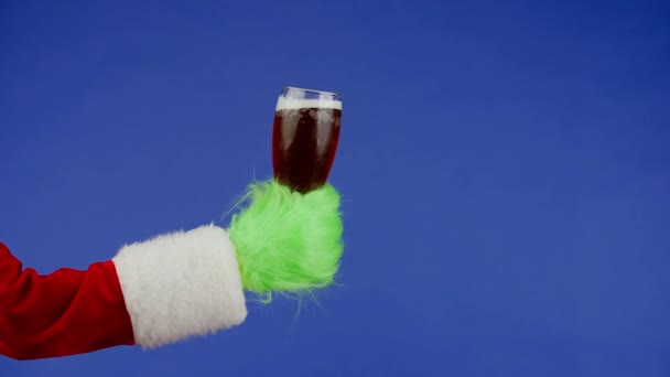 緑色のハイレッドの手は 隔離された青色の背景に濃いビールのグラスを保持しています ギフトスナッチャーコスプレ クリスマスと新年のお祝いコンセプト ブルースクリーン クロマキー — ストック動画