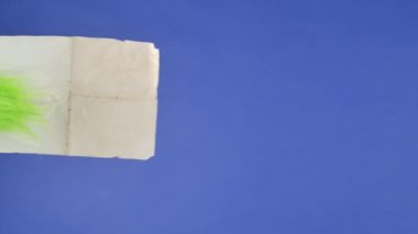 Grinchs 'in yeşil saçlı eli mavi izole bir arka planda boş bir vintage kraft kağıdı tutuyor. Hediye Hırsızı Kostümü. Noel ve Yeni Yıl kutlaması konsepti. Mavi ekran, krom anahtar