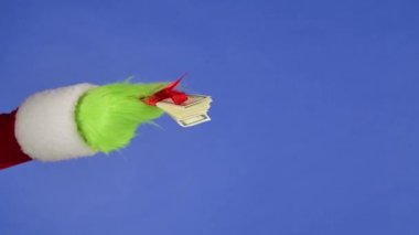 Yeşil saçlı Grinch el, izole bir arka planda kırmızı bir fiyonka sarılı bir tomar para tutuyor. Reklamınız için bir yer. Noel ve yeni yıl kutlaması konsepti. Mavi ekran, krom anahtar