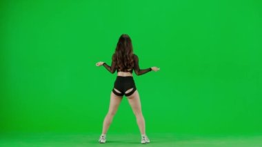 Yeşil arkaplanda, kromakey genç bir kadın duruyor. Sırtı kameraya dönük, gösterişli kıyafetler giyiyor ve twerk dansı yapıyor. Seksi, plastik..