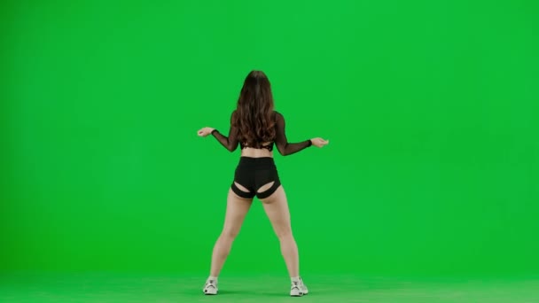緑色の背景のフレームには 染色体は若い女性を立っています 彼女は背中をカメラに向け 服を明らかにし ダンスの動きを示している 彼女はセクシーで プラスチック — ストック動画