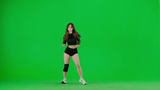 緑色の背景に囲まれて 染色体は若い女性を立っています 彼女はカメラを覗き込んで服を着て ツワルケのダンスを披露する シェイス セクシー プラスチック スローマウント — ストック動画