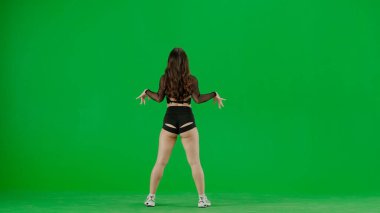 Yeşil arkaplanda, kromakey genç bir kadın duruyor. Sırtı kameraya dönük, gösterişli kıyafetler giyiyor ve twerk dansı yapıyor. Seksi, plastik..