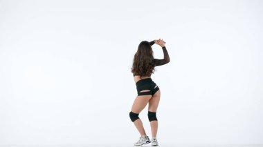 Çerçevede beyaz bir arka planda genç ve narin bir kadın duruyor. Sırtı kameraya dönük, gösterişli kıyafetler giyiyor ve twerk dansı yapıyor. Seksi, plastik..