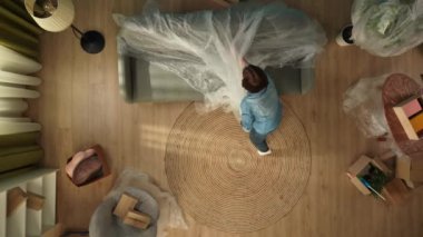 Yeni ev ve gayrimenkul yaratıcı reklam konsepti. Taşınma ve tahliye. Oturma odasının en iyi manzarası. Kadın odaya giriyor, koltuktan film alıyor ve toz fırçasıyla temizliyor..