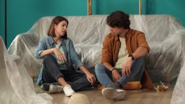 Yeni ev ve gayrimenkul yaratıcı reklam konsepti. Taşınma ve tahliye. Oturma odasını kapatın. Yeni dairenin zemininde oturan bir çift, kadını meyvelerle besleyen bir adam, mutlu bir sohbet..