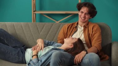 Yeni ev ve gayrimenkul yaratıcı reklam konsepti. Taşınma ve tahliye. Oturma odasını kapatın. Yeni dairede kanepede oturan bir adam, uyluklarında uzanan bir kadın, mutlu bir kahkaha..