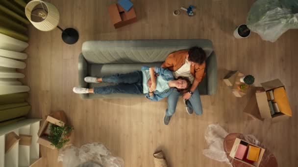家庭温暖和房地产创意广告的概念 搬迁和驱逐 客厅的顶视图 男人坐在新公寓的沙发上 女人躺在他的大腿上 开心地谈笑风生 — 图库视频影像