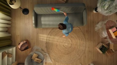 Yeni eve taşınma ve kiralama konsepti. Taşınmak ve taşınmak. Oturma odasının en iyi manzarası. Odadaki tüm mobilyaları toz fırçasıyla temizleyen kadın..