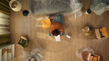 Yeni eve taşınma ve kiralama konsepti. Taşınmak ve taşınmak. Oturma odasının en iyi manzarası. Yerde oturan adam elinde tahliye ve borç kağıtları, bunalımlı bakışlar..