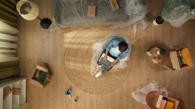 Yeni eve taşınma ve kiralama konsepti. Taşınmak ve taşınmak. Oturma odasının en iyi manzarası. Bir kadın dizüstü bilgisayarda çalışıyor. Bir sürü kutuyla dolu bir odada..