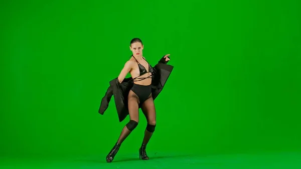 框架在绿色的背景上 铬钥匙 穿着敞开的衣服和夹克的年轻女人 把它往下拉 演示一种舞蹈向高跟鞋的方向发展 她性感 有节奏 — 图库照片