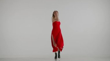 Beyaz, gri bir arka planda çerçevelenmiş. Genç bayan, yüksek topuklara doğru dans hareketlerini gösteriyor. O güzel kırmızı bir elbise ve yüksek topuklu ayakkabılar giyiyor. Seksi, ritmik, plastik. Orta boy..