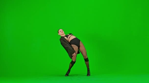 緑色の背景に 染色体を塗りました オープンドレスとジャケットに立っている若いスレンダーの女性 ハイヒールの方向にダンスの動きを示しています 彼女はセクシーで プラスチックで リズム的だ ミディアムショット — ストック動画