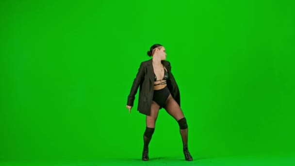 框架在绿色的背景上 铬钥匙 身材苗条的年轻女子穿着敞开的衣服和夹克站在那里 演示一种舞蹈向高跟鞋的方向发展 她是性感的 — 图库视频影像