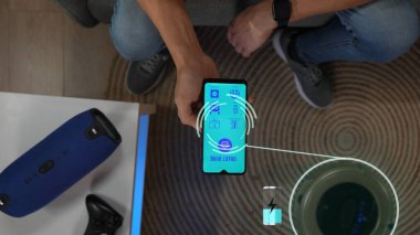 Akıllı ev teknolojisi yaratıcı konsepti. Üst görüntü kanepede adamın yakın çekimi, akıllı telefonu elinde tutarken aygıtlar için bir uygulama, temizleyiciyi açarken. Nesne üzerindeki bilgisel dijital resim.