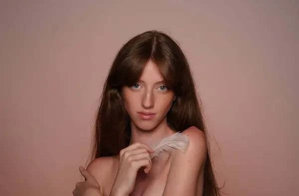 一个女人用羽毛摸她的皮肤 背景为褐色的演播室中的精液女子的肖像 柔软而光滑的身体 皮肤护理概念 — 图库照片