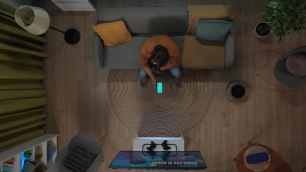 智能家居和现代技术的概念 房间里的男性画像 男人坐在房间沙发上 用智能手机上的应用程序打开家用电器 电视和游戏机的头像 — 图库视频影像