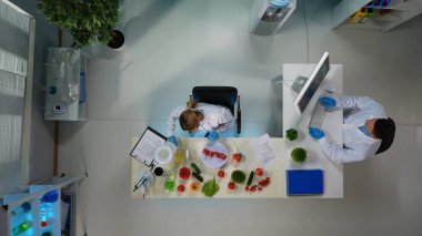 Yukarıdaki çerçeve bir laboratuvarda oturan bilim adamlarını gösteriyor. Bir kadın araştırma yapıyor, test ediyor, yakınında bulunan domates ve sebzelerden örnekler alıyor. Bir adam bilgisayarda yazı yazıyor. Genel plan.