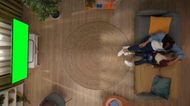Aile bağı ve ebeveynlik yaratıcı konsepti. Evde birlikte vakit geçiririz. Üst kattaki daire manzarası, anne ve oğlu kanepede oturup tablet TV 'de krom renkli yeşil ekranlı video izliyorlar..
