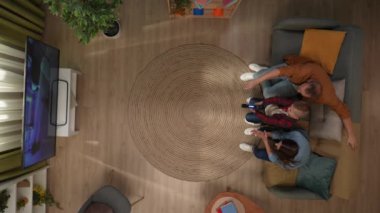 Aile ilişkileri ve ebeveynlik reklamları. Ailecek vakit geçireceğiz. Oda manzarası, anne baba ve oğul koltukta oturuyor, çocuk video oyunu oynuyor, ebeveynler çocuğun kazanmasına yardım ediyor..