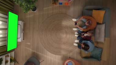Aile ilişkileri ve ebeveynlik reklamları. Oturma odasının en üst görüntüsü, anne-baba ve oğul kanepede oturup TV 'de krom anahtar yeşil ekranla oyun oynuyorlar, çocuk oyunu kazandı..