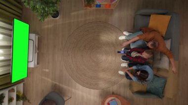 Aile ilişkileri ve ebeveynlik reklamları. Oturma odasının en üst görüntüsü, anne baba ve oğul koltukta, video oyunu oynayan çocuk televizyonda krom anahtar yeşil ekranlı silah kumandası kullanıyor..