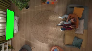 Aile ilişkileri ve ebeveynlik reklamları. Oturma odasının en üst görüntüsü, koltukta oturan baba ve oğul, TV 'de krom renkli yeşil ekran ile video oyunu oynayan çocuk..