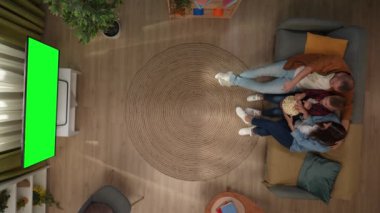 Aile ilişkileri ve ebeveynlik reklamları. Oturma odasının en iyi manzarası. Anne, baba ve oğul kanepede oturup, krom renkli yeşil ekranlı televizyon izleyip patlamış mısır yiyip sohbet ediyorlar..