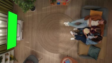 Aile ilişkileri ve ebeveynlik reklamları. Oturma odasının en iyi manzarası anne baba ve oğul kanepede oturup patlamış mısır yiyor, televizyonda krom renkli yeşil ekranlı korku filmi izliyorlar..