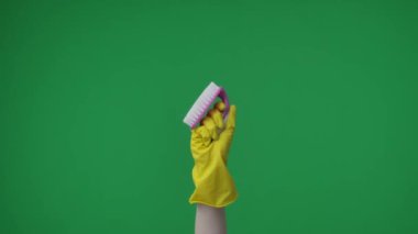 Yeşil arka plandaki çerçevede, sarı kauçuk eldivenli topal bir kadın eli bir fırçayı tutuyor ve gösteriyor. Temizlik ve temizlik için kullanılır. İşte reklamınız burada. Orta çerçeve.