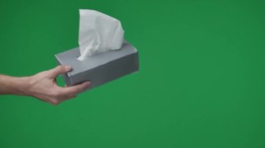 Yeşil arkaplana yakın çekim, kromakey. İki kişi. Bir erkek bir kutu mendili tutar ve uzatır, manikürlü bir kadın elini uzatır. Yardım ve bakım koşullarını gösterin..