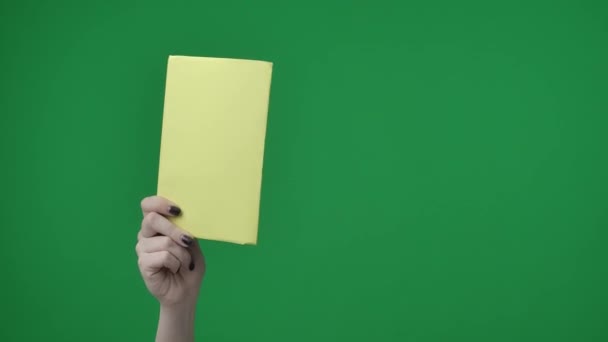 画框的特征是一个有着绿色背景的女人的特写 一只手握着一张空的 长方形的 黄色的A4纸片的女人的手 她把它指向摄像机 — 图库视频影像