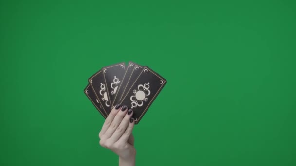在一个绿色背景的框架内 一只手拿着塔罗牌或扑克牌的扇子的女人 他们用图案朝外看相机 有人在抽一张牌 — 图库视频影像