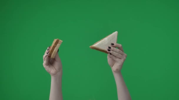 グリーンバックのクローズアップショットで 女性の手は三角形の形をした2つのパン粉を持っています 彼女はカメラに手を伸ばした 暗くて軽いピースのペストリーを示しています — ストック動画