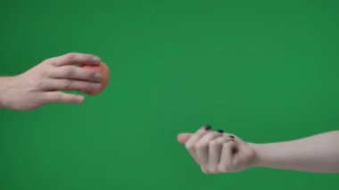 Yeşil arkaplana yakın çekim, kromakey. İki kişi. Manikürlü bir kadın elmayı tutar ve tutar. Adamın biri elini kapatıyor. Paylaşıyorlar, bir şeyler paylaşıyorlar..