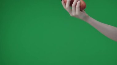 Yeşil arkaplana yakın çekim, kromakey. Bir kişi. Manikürlü bir kadın iki elma tutar ve birine elini uzatır. Muhtemelen birinin onları almasını bekliyordur..