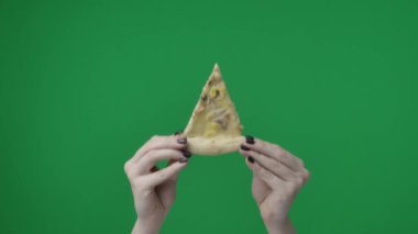 Yeşil kromakey arkaplanına yakın çekim. Bir kadının eli, bir dilim pizzayı ellerinde malzemelerle tutuyor. Kameraya gösteriyor, gösteriyor, paylaşıyor..