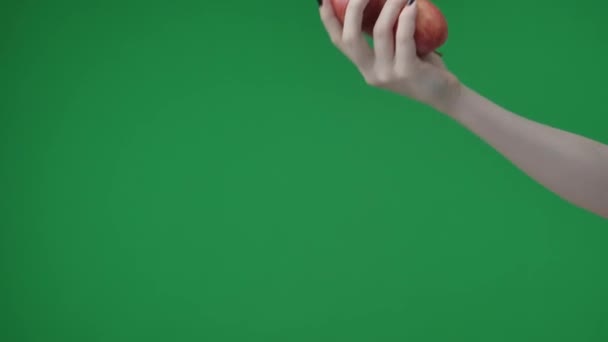 緑色の背景にある クロメイクの写真です 一人で マニキュアを持つ女性はリンゴを2つ持っていて 誰かに手を伸ばします おそらく誰かがそれらを取るのを待っている — ストック動画