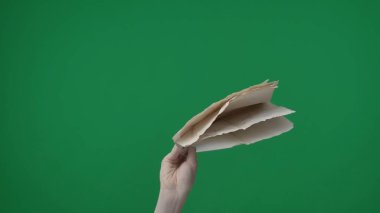 Yeşil arka planda çerçevelenmiş, kromakey. Manikürlü bir kadının eli küçük bir yığın buruşmuş beyaz kağıt tutar. Kameraya bakan tarafıyla onları yukarıda tutuyor. Orta çerçeve