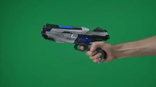 In a shot on a green background, a chromakey male hand that holds, holds out a plastic gun, a blaster, he pulls the trigger and points somewhere. Here can be your advertising. Medium shot.