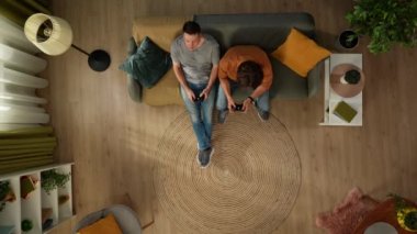 Evde homoseksüel bir çiftin en iyi görüntüsü. Kanepede oturuyorlar, ellerinde oyun kağıtlarıyla video oyunu oynuyorlar, eğleniyorlar ve birbirleriyle konuşuyorlar. LGBT, eşitlik, eğitim.