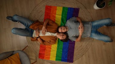 Eşcinsel, biseksüel, panseksüel, transseksüel bir çiftin LGBT bayrağının üzerinde yatıp sevgiyi, eşitliği, özgürlüğü teşvik etmek için kameraya bakmasının en iyi görüntüsü. Eğitimsel içerik, aşk özgürlüğü, gurur.