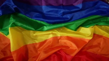 Üst görüntü, çerçevenin zıt köşelerinden el sıkışmaya çalışan iki erkeğin el sıkışmasını çekiyor. Arka planda LGBT bayrağı var. Eğitim içeriği, eşitlik, homoseksüellik, gurur.