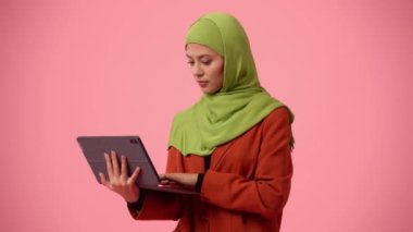 Orta ölçekli izole bir video, tesettür ve duvak takan çekici bir genç kadını çekiyor. Elinde bir tablet, dizüstü bilgisayar var, bir şeyler yazıyor. Kültürel çeşitlilik, iş ve eğitim, reklam.
