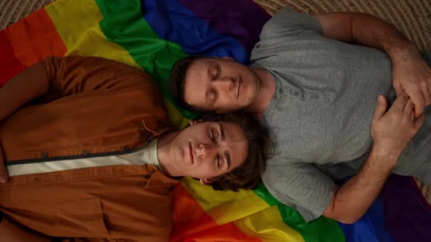 同性愛者 バイセクシャル パノラル トランスジェンダーのカップルがLgbtの旗の上に横たわり 自由を奨励するためにカメラに目を開いて微笑むトップビューショット 教育コンテンツ — ストック動画
