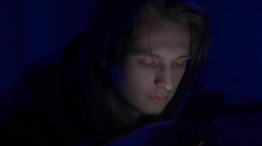 Kaş piercingli genç bir adam, gece geç saatlerde evde uzanmış, akıllı telefon kullanarak dinleniyor, sohbet ediyor ve mesajlaşıyor. Adam cep telefonunu kapatıp yatmaya gidiyor.