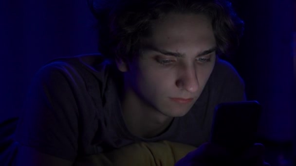 若い男性が夜に自宅でベッドで寝ているスマートフォンにテキストを送っている その男は電話を切って寝る インターネット コミュニケーション 人々のコンセプト — ストック動画