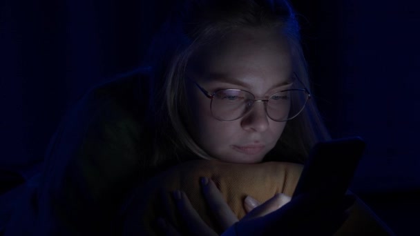 眼鏡をかけた若い女性は 自宅で寝ているスマートフォンにテキストを送っている ある女性が電話を切って寝る インターネット コミュニケーション 人々のコンセプト — ストック動画